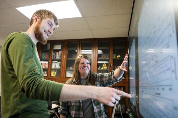 Student and staff member observing graph data on a smartboard